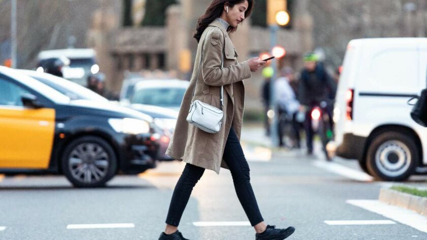 Eine junge Frau schaut auf ihr Handy und überquert dabei eine Straße