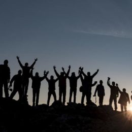 Silhouetten von einer Gruppe von Menschen bei Offsite-Tour mit Rucksäcken vor Sonnenuntergang