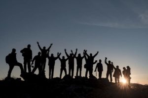 Silhouetten von einer Gruppe von Menschen bei Offsite-Tour mit Rucksäcken vor Sonnenuntergang