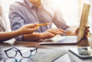 Zwei Personen in einer Besprechung mit Laptop, Stift und Unterlagen