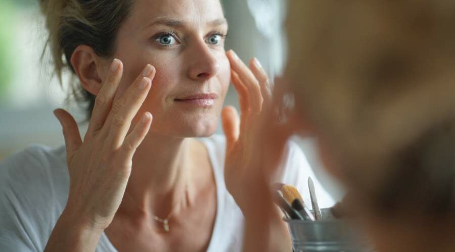 Close-up auf das Gesicht einer Frau, die sich im Spiegel betrachtet und die Haut ihrer Wangenknochen berührt