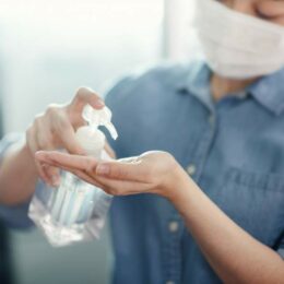 Frau mit Mundnasenschutz in Büroumgebung desinfiziert sich die Hände