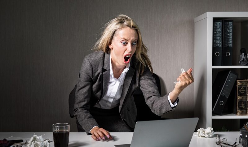 Wuetende Frau ist genervt von Werbung am Arbeitsplatz und schreit ihren Computer an