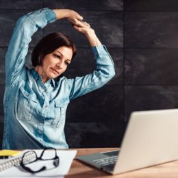 Frau macht Stretchinguebungen am Schreibtisch