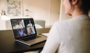 Person im Homeoffice sitzt an Tisch im Wohnbereich zu Hause in einem Online-Meeting mit vier weiteren Personen