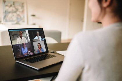 Person im Homeoffice sitzt an Tisch im Wohnbereich zu Hause in einem Online-Meeting mit vier weiteren Personen