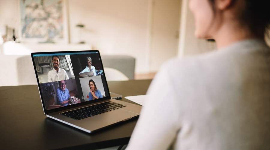 Person im Homeoffice sitzt an Tisch im Wohnbereich zu Hause in einem Online-Meeting mit vier weiteren Personen