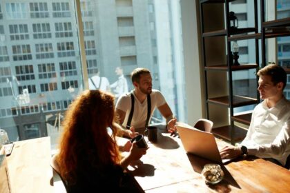 Junge Mitarbeitende im Team sitzen am Tisch während der Kaffeepause in einem hellen modernen Büroraum