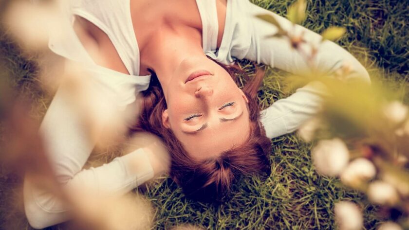 Frau liegt entspannt mit geschlossenen Augen im Gras