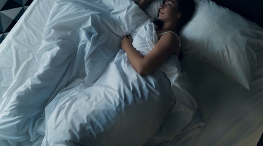 frau mit guter schlafhygiene schlaeft in bett mit weißer bettwaesche