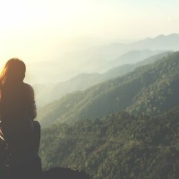 Silhouette einer Frau, die auf einem Berggipfel die Aussicht genießt