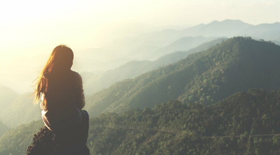 Silhouette einer Frau, die auf einem Berggipfel die Aussicht genießt