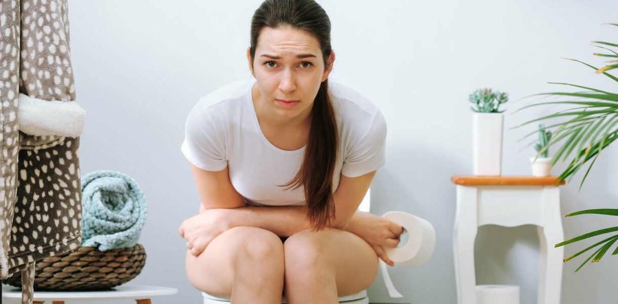 Frau sitzt mit Verstopfung auf der Toilette wegen schlechter Darmgesundheit