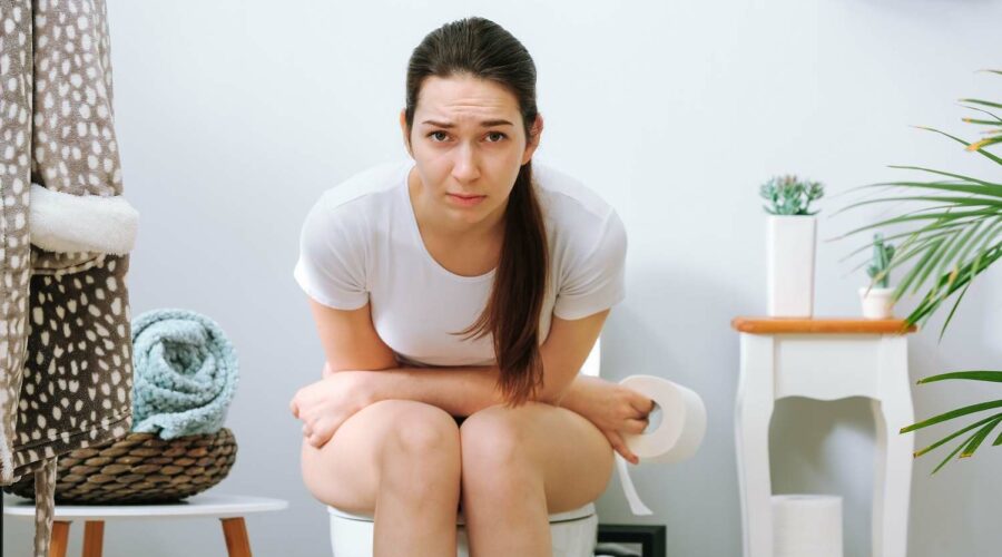 Frau sitzt mit Verstopfung auf der Toilette wegen schlechter Darmgesundheit