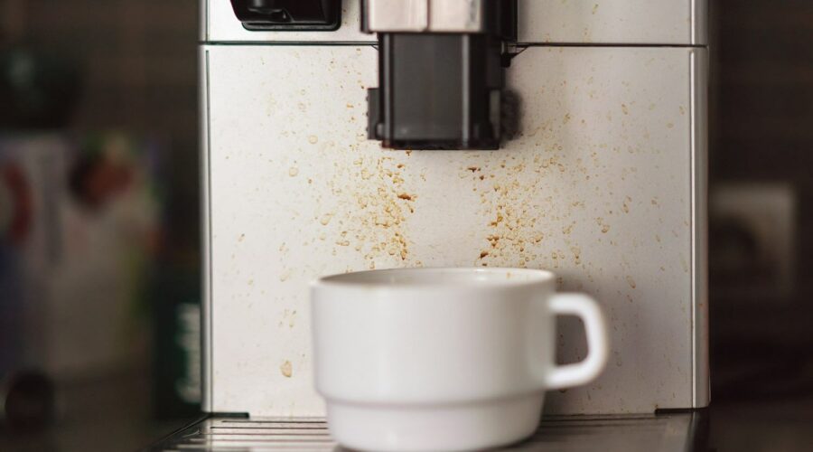 Dreckige Kaffeemaschine im Büro mit weißer Tasse spricht nicht für Hygiene am Arbeitsplatz