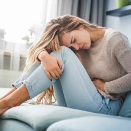 Frau mit Blutungsstörungen krümmt sich auf dem Sofa mit starken Regelschmerzen