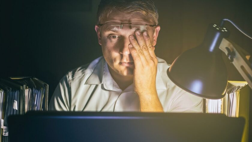 Mann sitzt im Dunkeln am Schreibtisch und leidet unter Konzentrationsschwäche